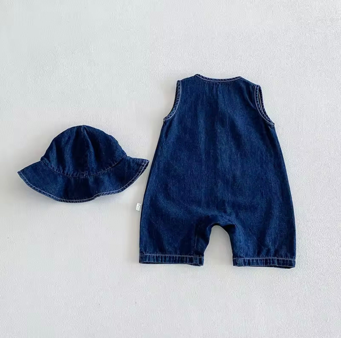 Blue denim romper and hat set on a light gray background