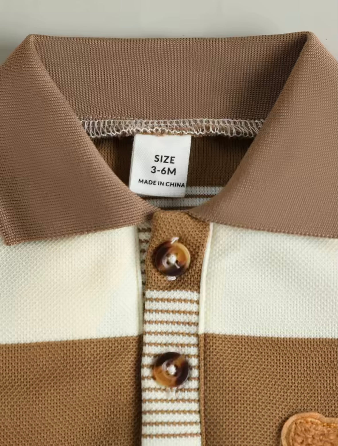 Close-up of a baby's striped polo shirt with a label showing size 3-6 months.
