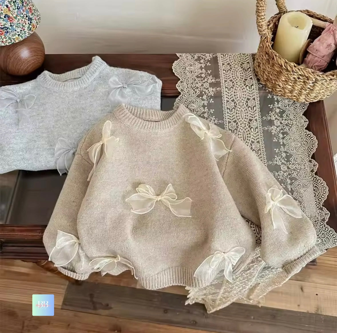 Two children's sweaters with bow details on a lace tablecloth.