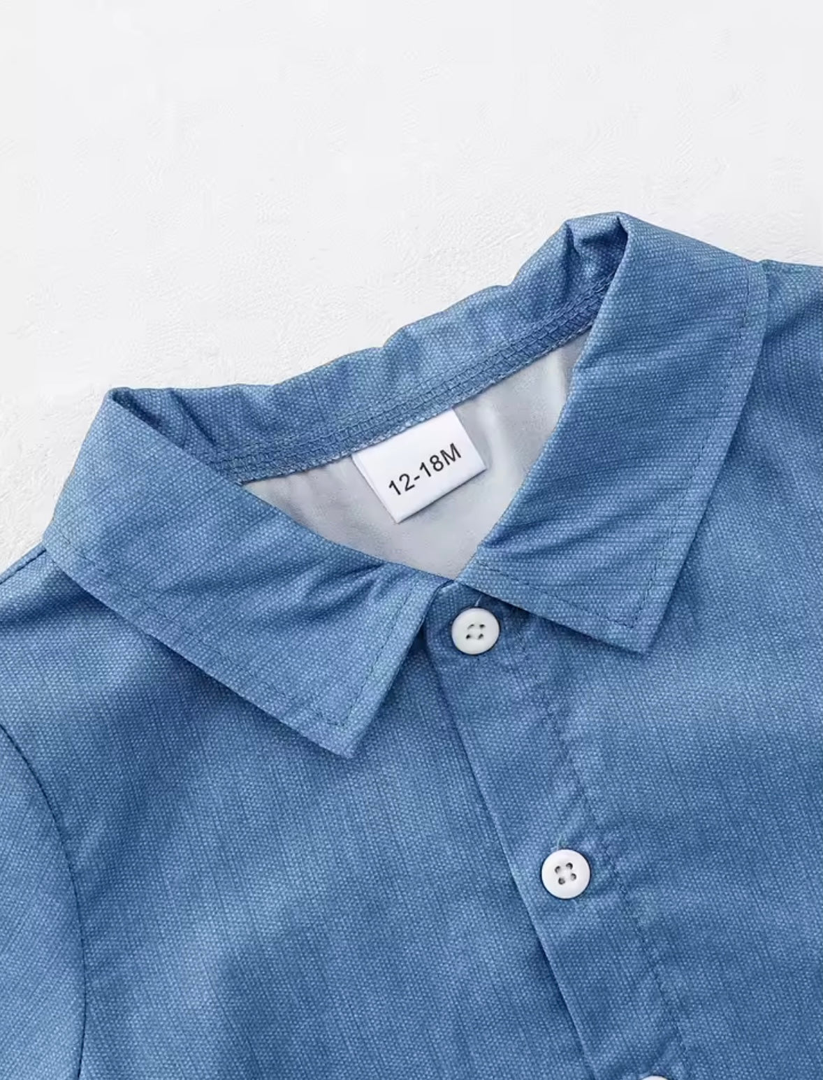 Close-up of a blue shirt collar with buttons and a visible size tag on a white background