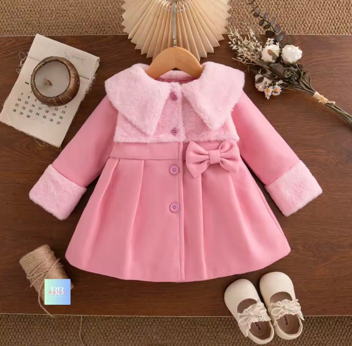 Pink children's coat with fur trim on a wooden surface, accompanied by shoes.