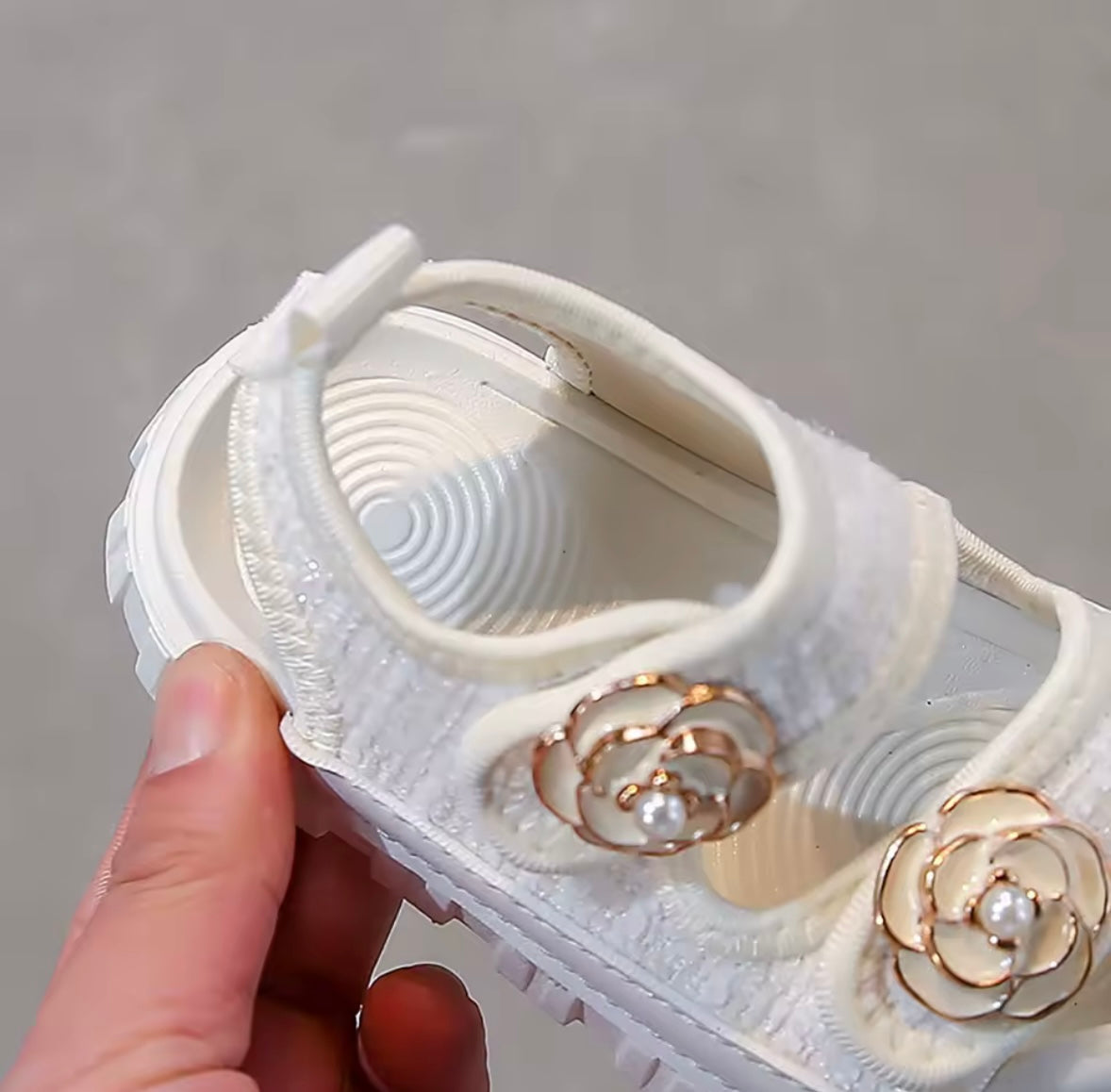 White sandal with gold floral designs held by a hand against a neutral background