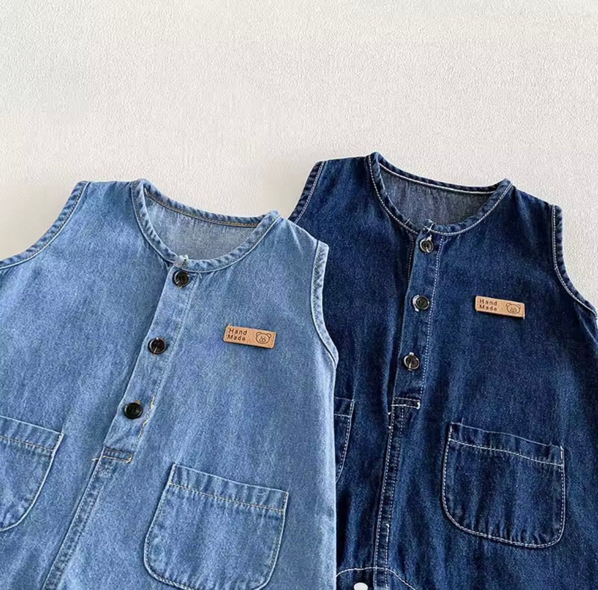 Two denim vests, one light blue and one dark blue, on a white background.