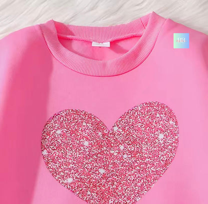 Pink sweatshirt with a glittery heart design on a light wooden surface