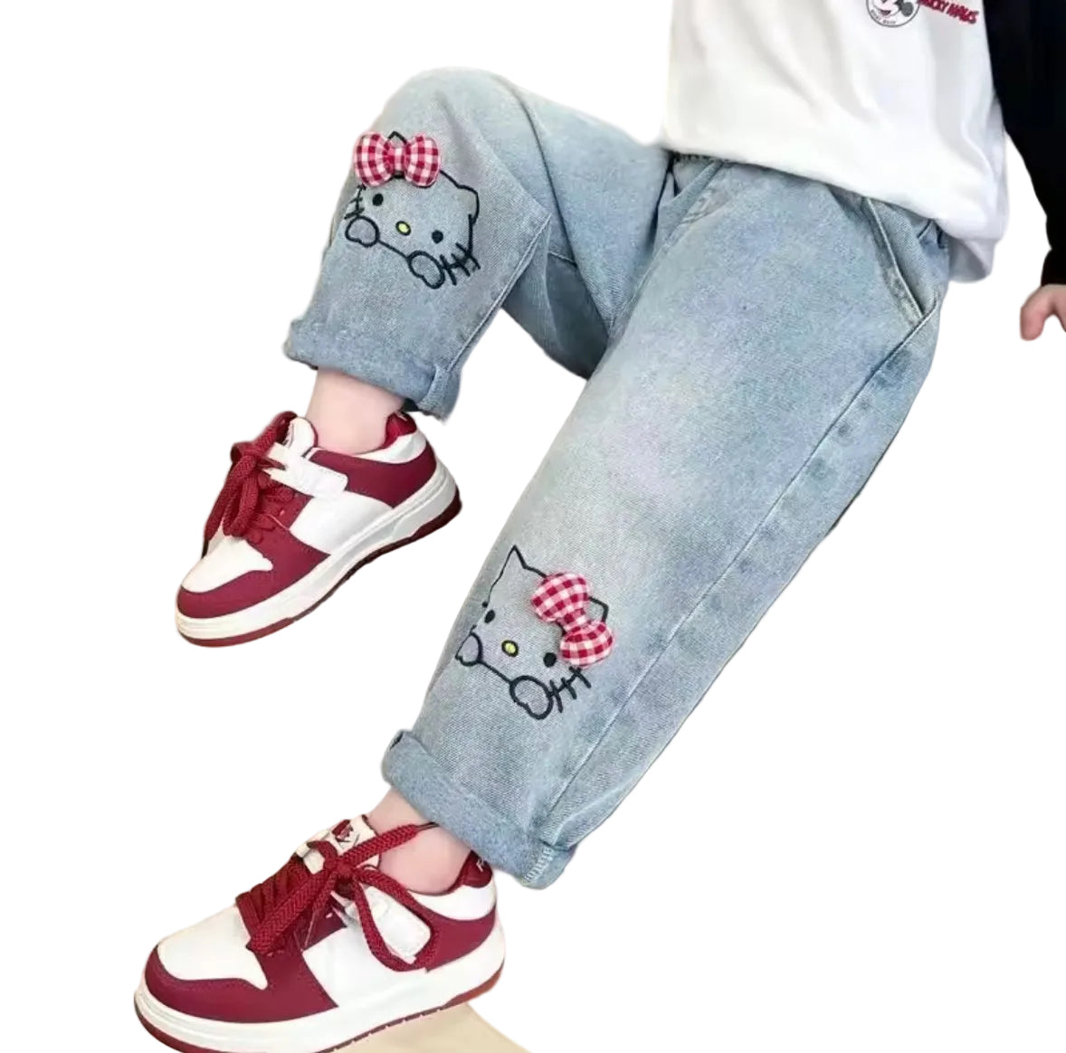 Children's jeans with cat face designs and red and white sneakers on a beige background