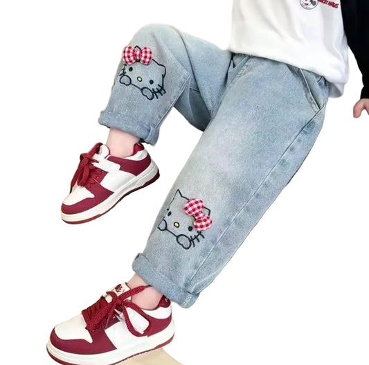 Children's jeans with cat face designs and red and white sneakers on a beige background
