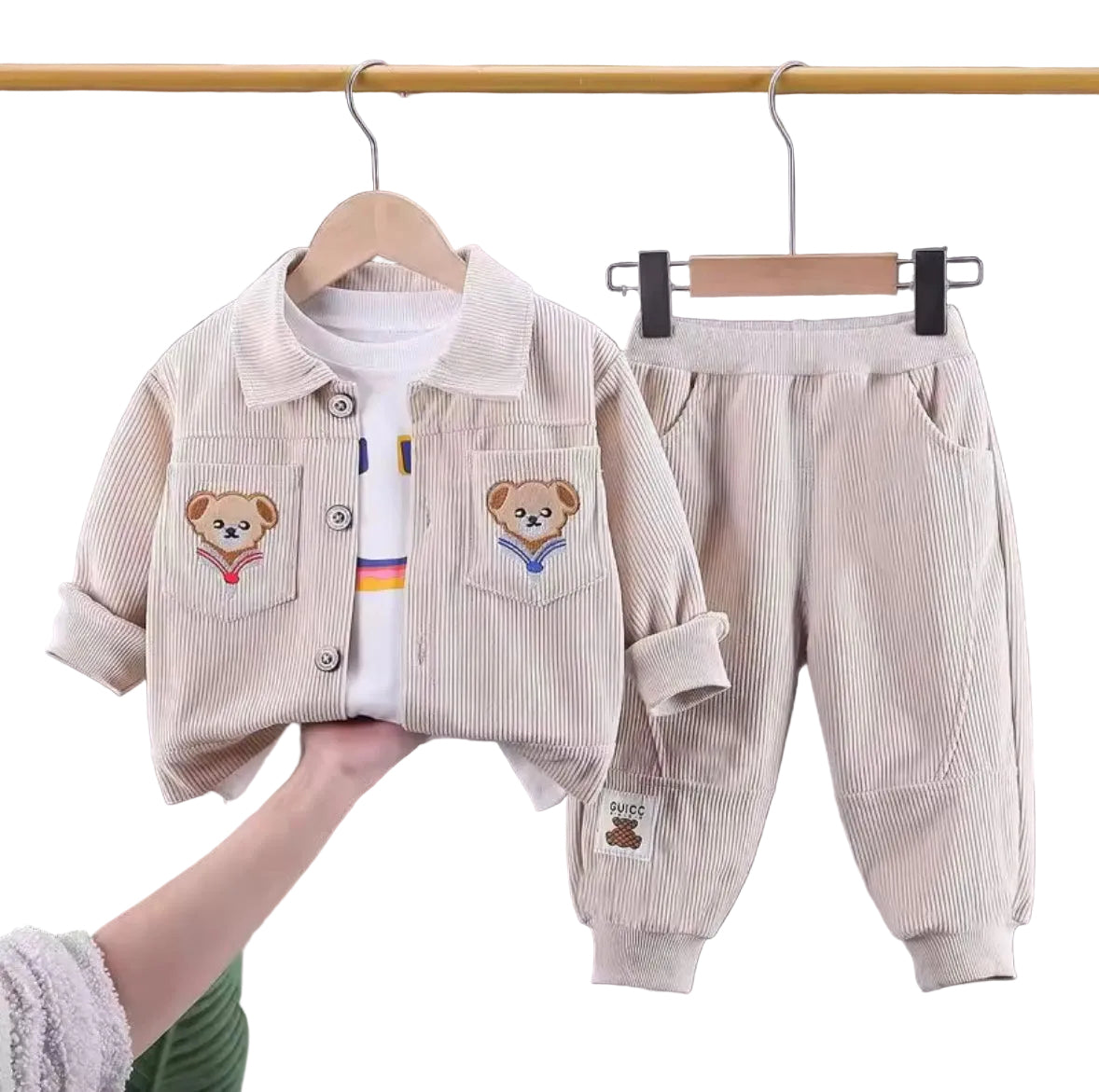Children's clothing set with jacket and pants on hangers against a neutral background