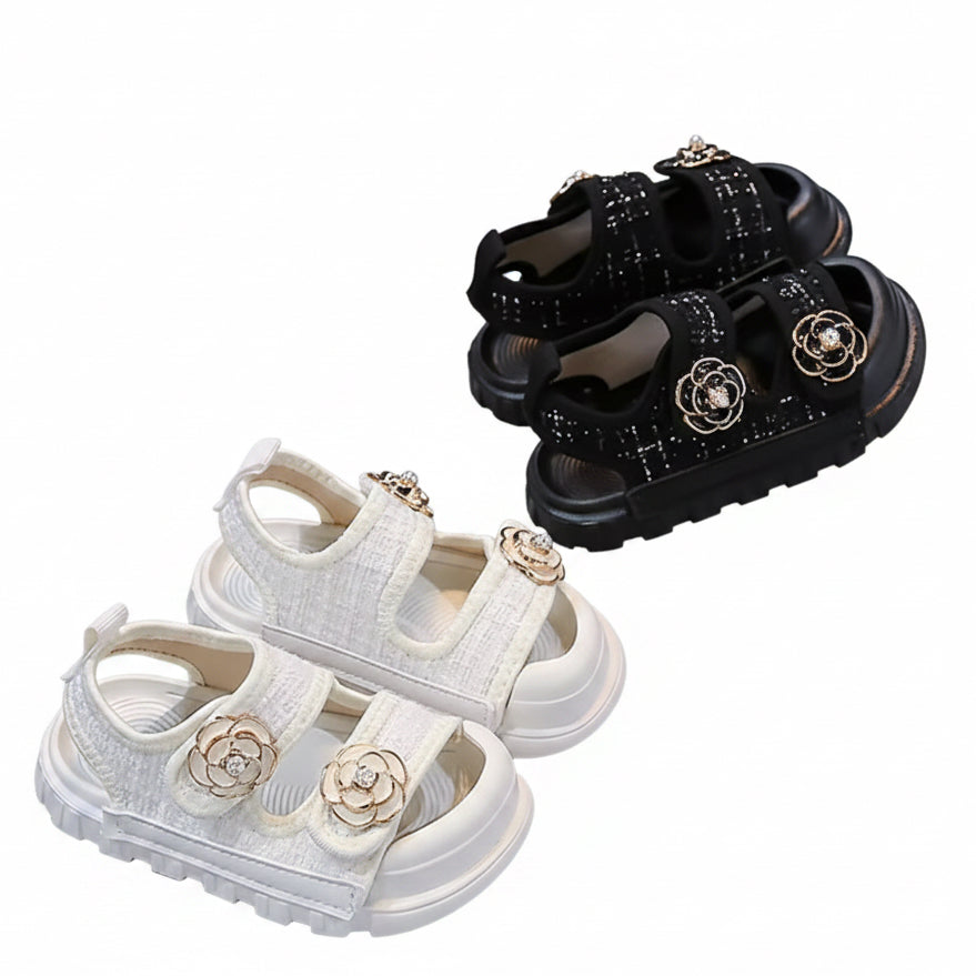 White and black sandals with floral embellishments on a gray surface.