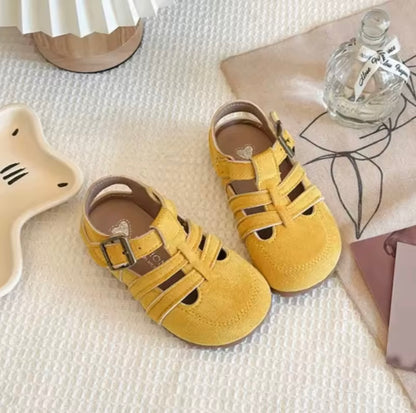 Yellow children's sandals on a textured surface with decorative items.