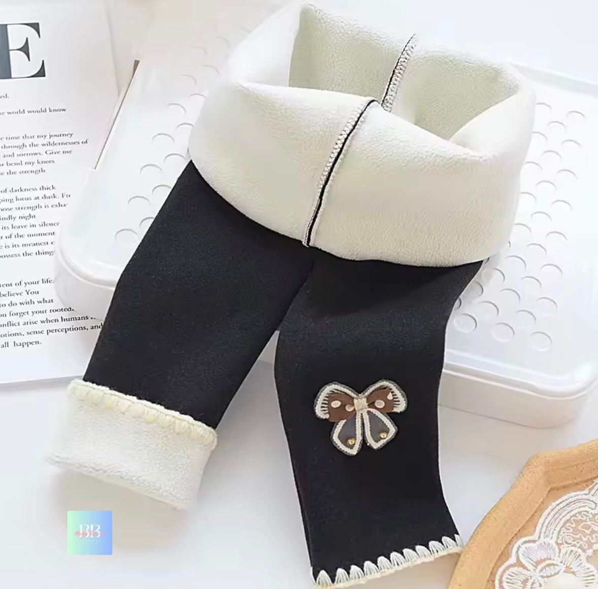 Black leggings with white fleece trim and a butterfly design on a white surface.