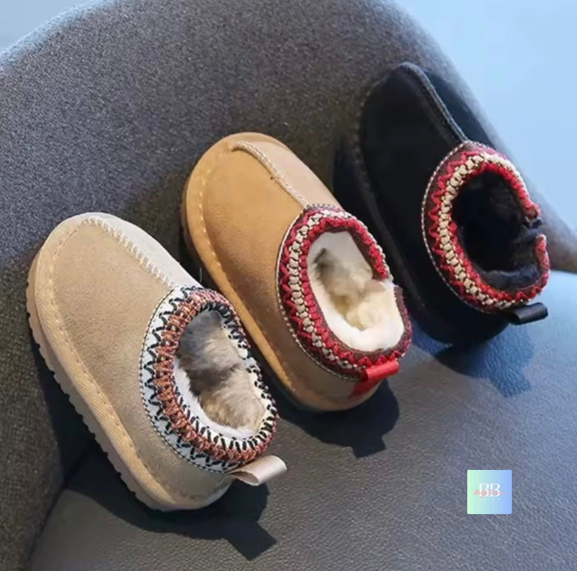 Three pairs of baby boots with knitted trim on a textured surface.