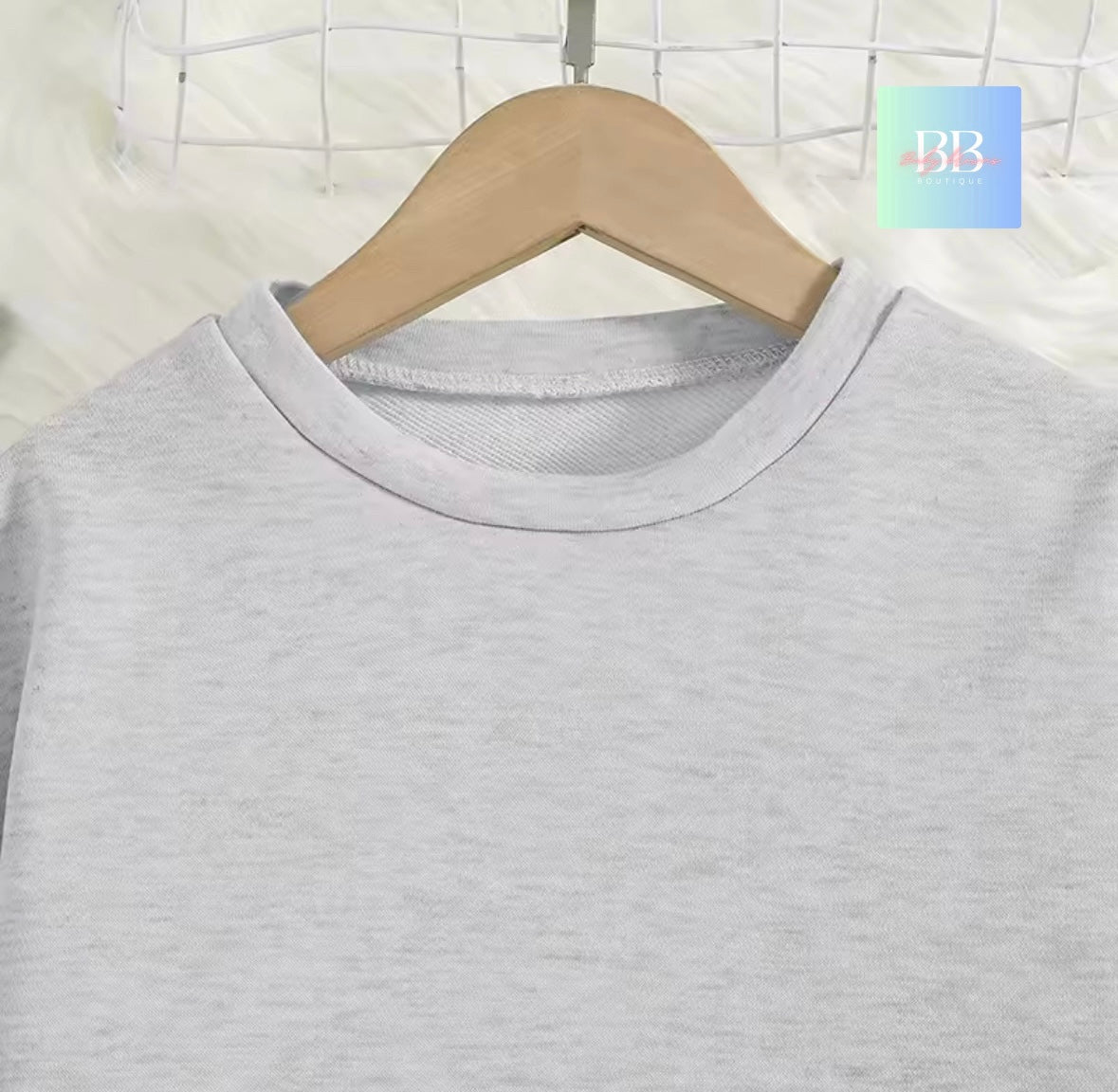 Gray t-shirt on a wooden hanger against a white grid background