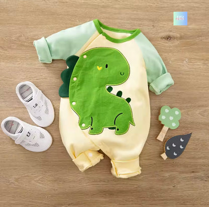 Baby romper with dinosaur design on a wooden surface, accompanied by baby shoes and a toy.
