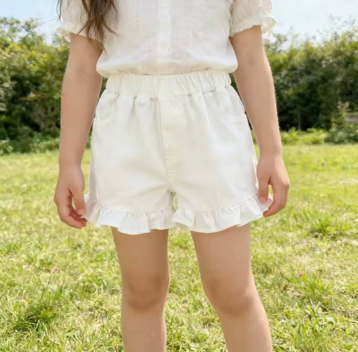 Person wearing white shorts with ruffles standing in a grassy field.
