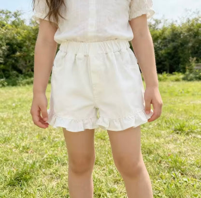 Person wearing white shorts with ruffles standing in a grassy field.