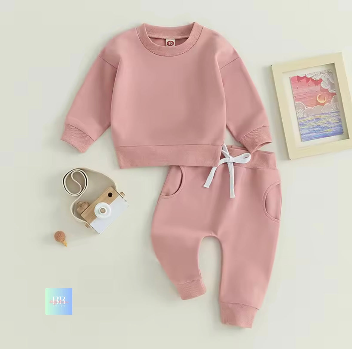 Pink children's sweatshirt and pants set on a light background with a small camera toy.