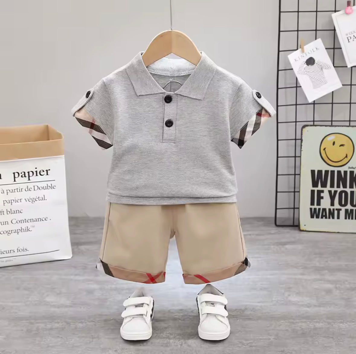 Children's outfit with gray polo shirt and beige shorts on a hanger against a neutral background.