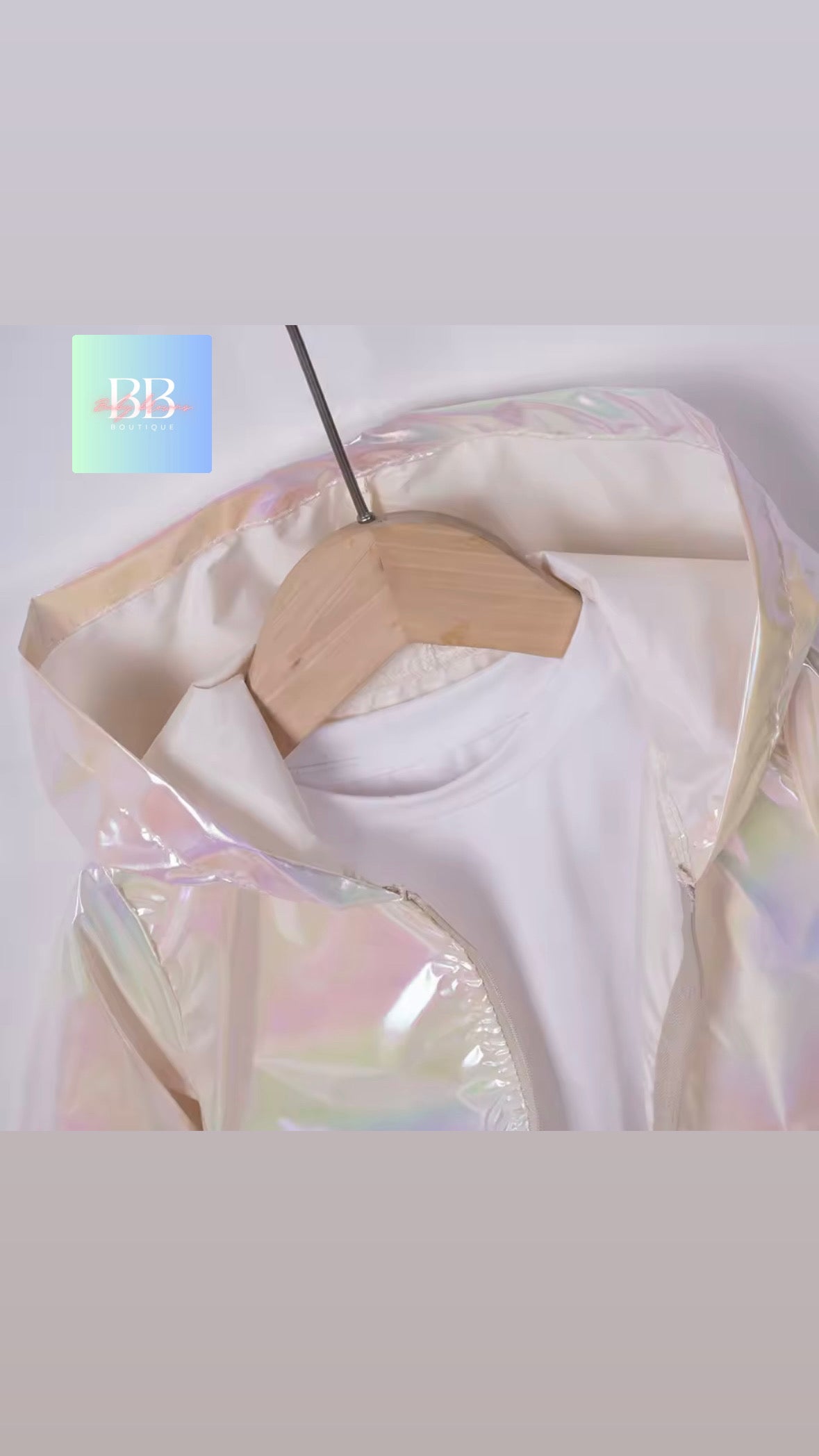 White top on a hanger with a transparent, iridescent cover against a light gray background