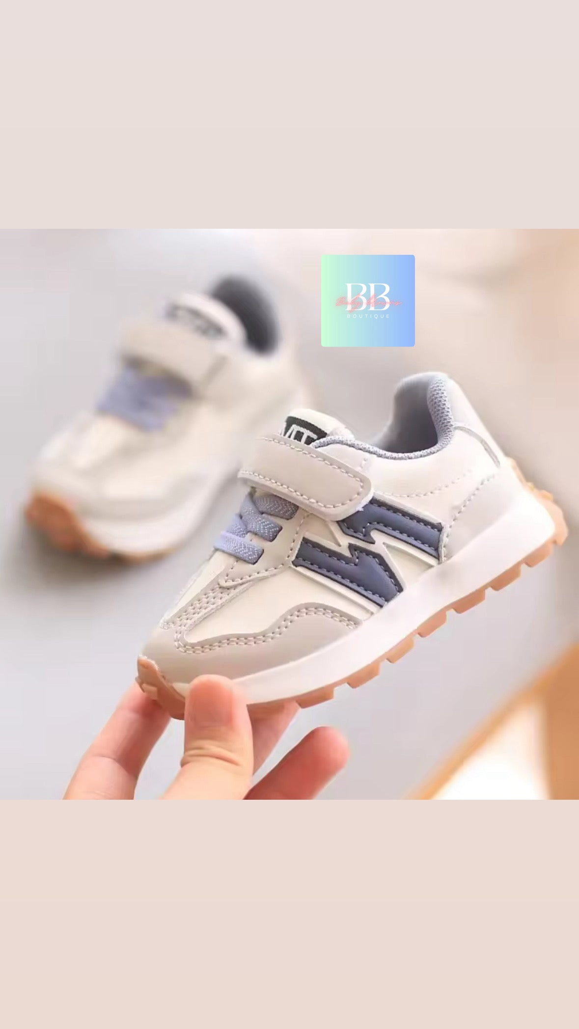 White and blue children's sneakers held by a hand against a light gray background