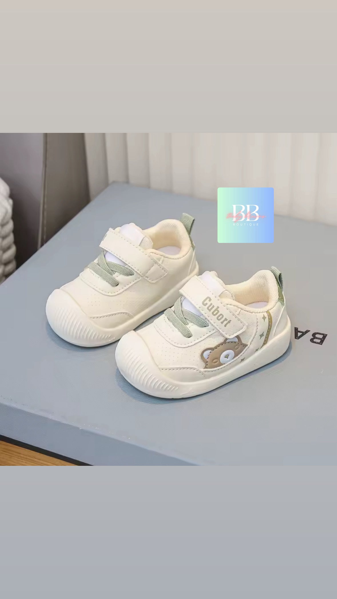 White children's shoes with green accents on a gray surface