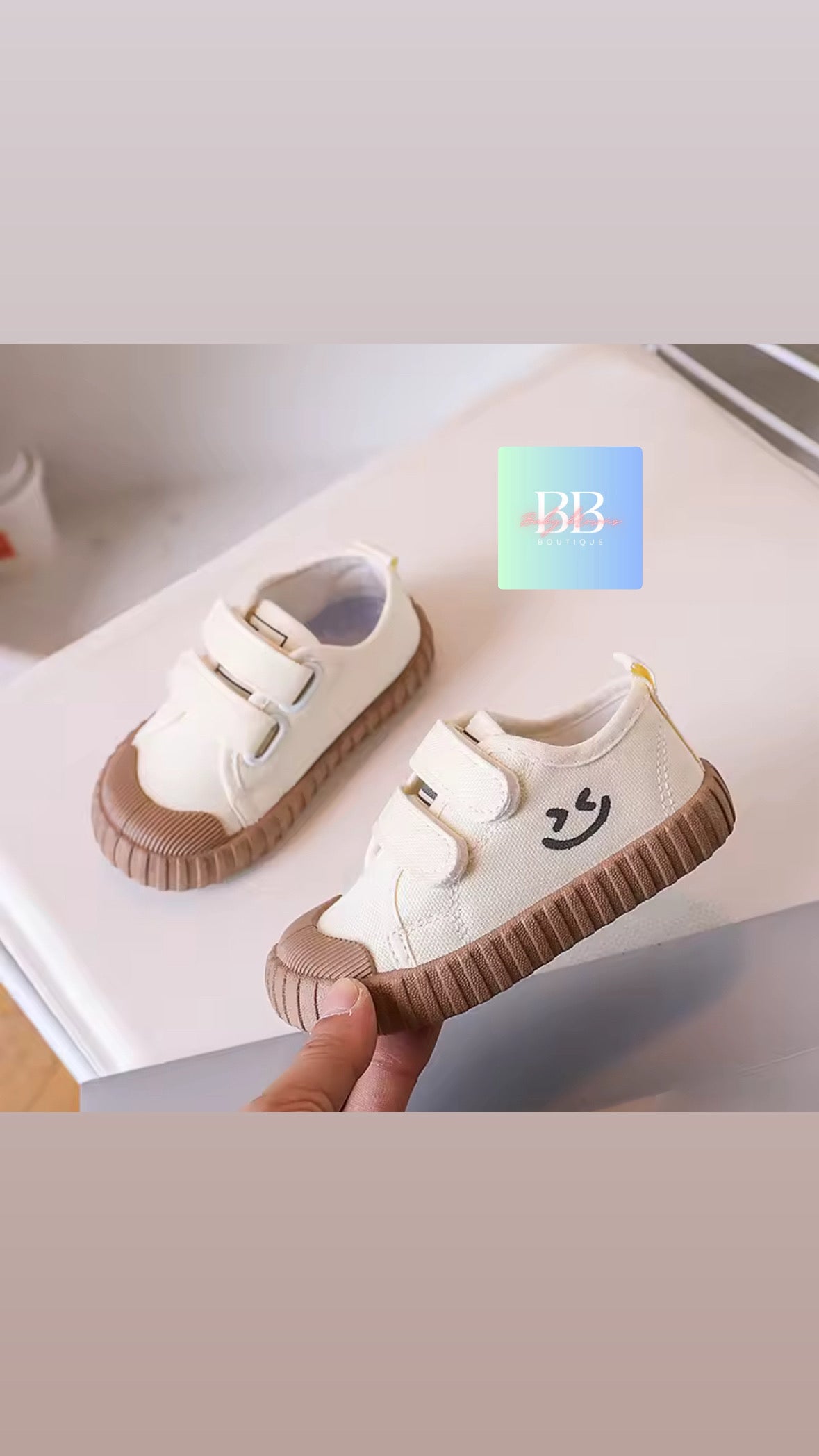 White children's shoes with brown soles held by a hand on a light background
