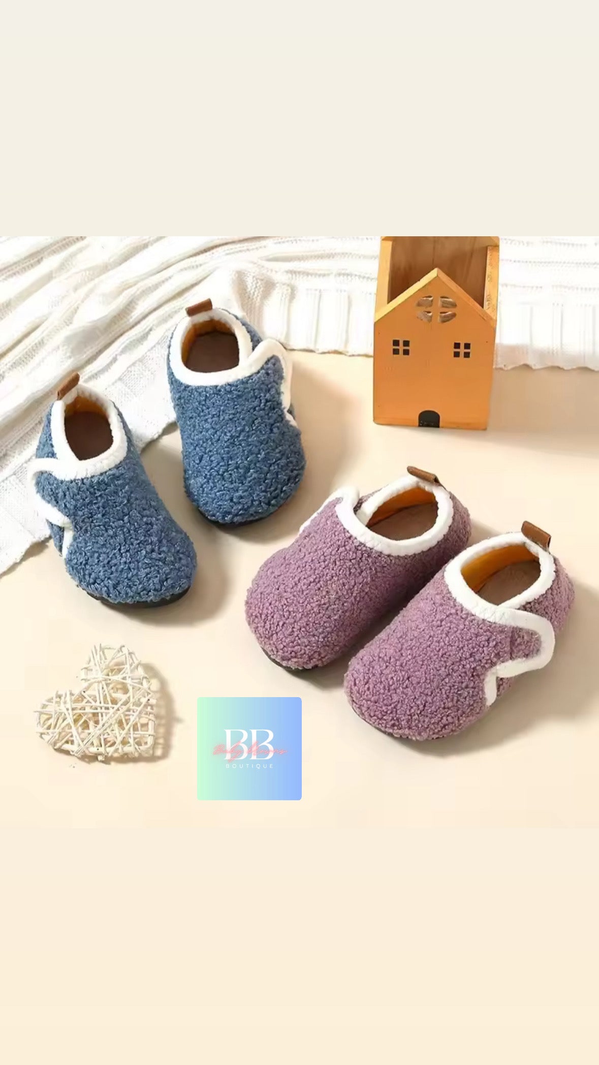 Pair of blue and purple children's slippers on a light background with a small wooden house and decorative heart.