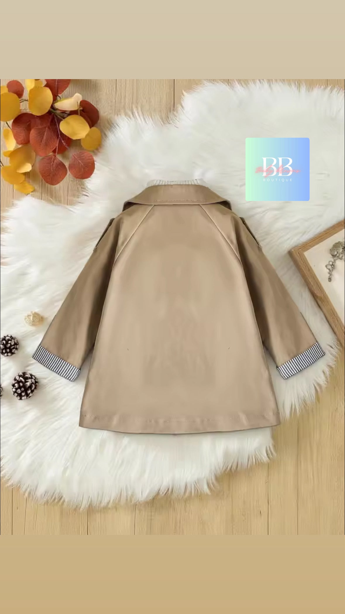 Beige coat with fur trim on a white fluffy surface with autumn leaves and a blue square in the corner.