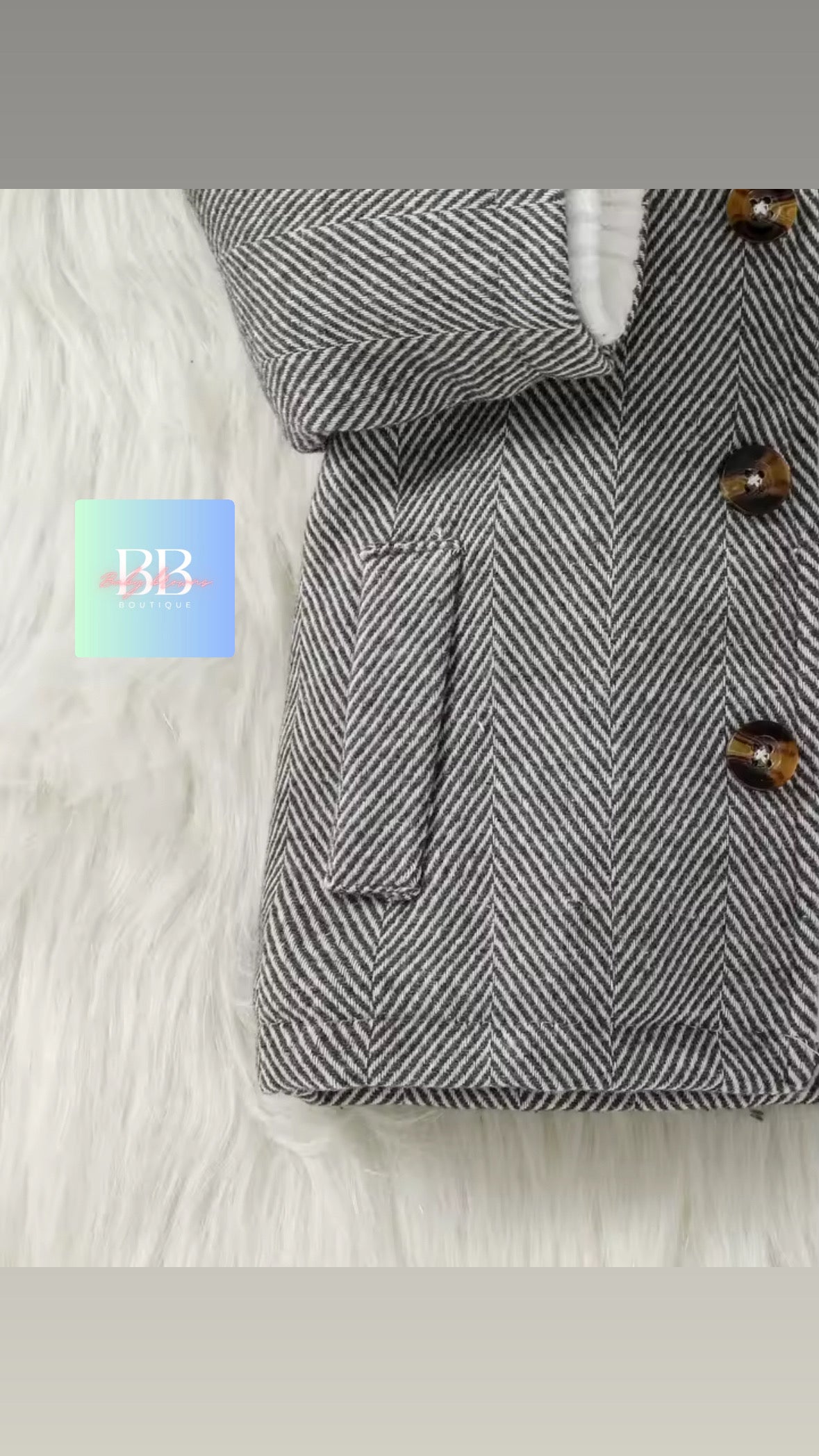 Gray herringbone coat with brown buttons on a white fur surface