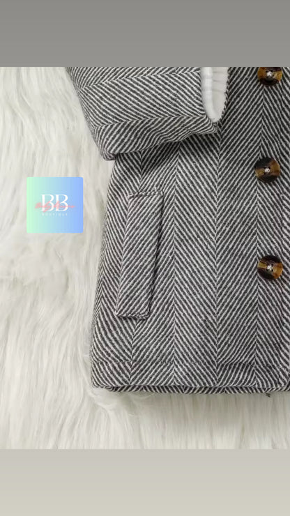 Gray herringbone coat with brown buttons on a white fur surface