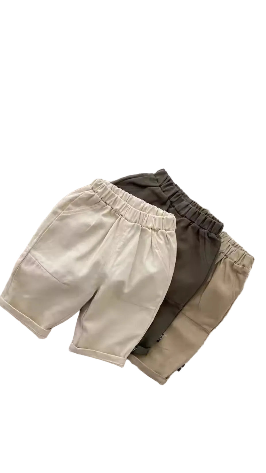 Three pairs of shorts in beige, brown, and green on a textured surface with a wicker basket in the background.