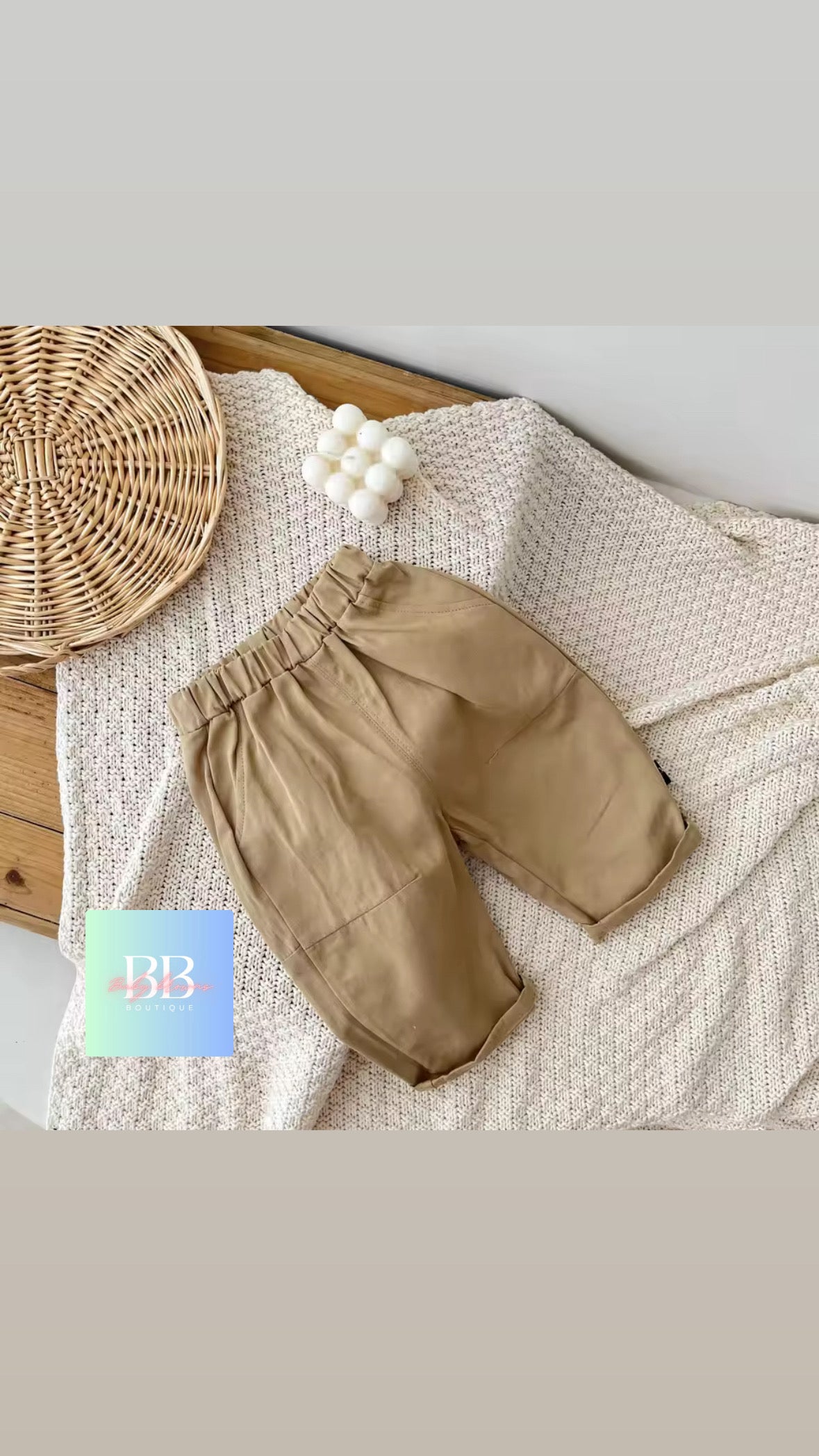 Beige pants on a textured surface with a woven basket and decorative items.