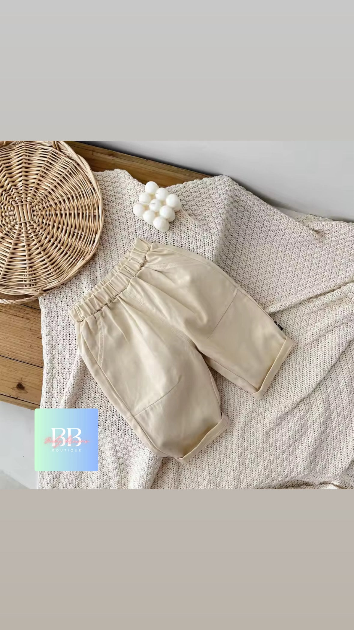 Beige baby pants on a textured surface with a woven basket and decorative items.